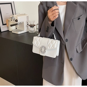 Close-up of white quilted handbag featuring a sparkling rhinestone buckle on the flap