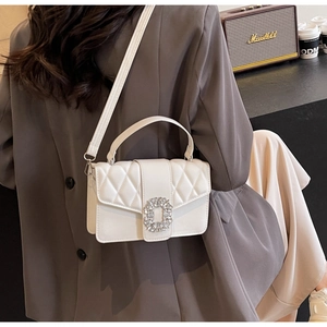 Detail of white quilted crossbody bag with a sparkling rhinestone buckle and chain strap