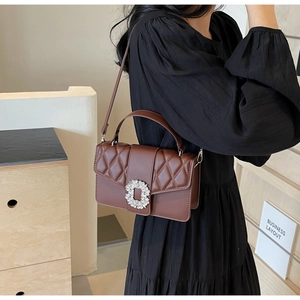 Close-up of brown quilted shoulder bag with oversized rhinestone buckle on black dress