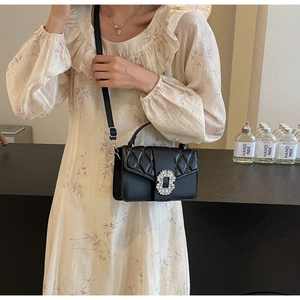 Detail of black quilted shoulder bag with large crystal buckle on a floral dress