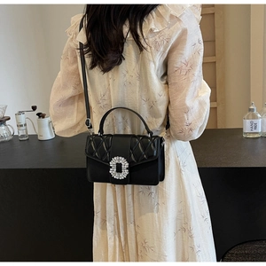 Detail of quilted black shoulder bag with luxury crystal buckle and elegant chain strap