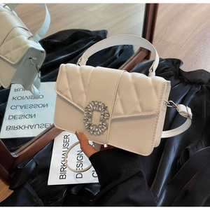 Detail showing the white quilted leather texture and large square rhinestone buckle on handbag