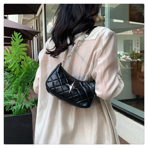 Close-up of black quilted shoulder bag with silver star emblem and metal chain strap