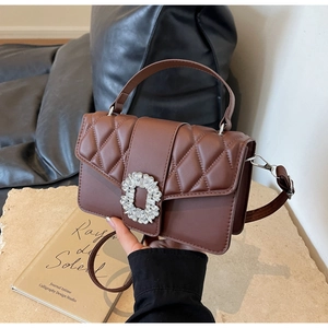 Detailed view of brown quilted bag with a luxury crystal buckle on stone pedestal
