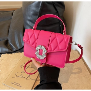 Detail of fuchsia quilted handbag featuring a large sparkling rhinestone buckle and slim strap