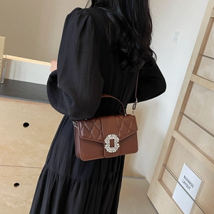 Dark brown leather shoulder bag with quilted details and a crystal buckle worn by a model
