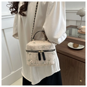 Close-up of cream woven bag with floral embroidery and gold chain strap on a model