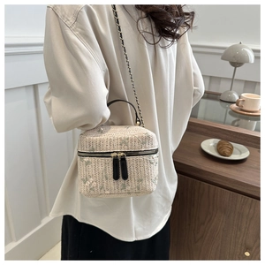 Detail of beige straw crossbody bag featuring floral embroidery and metal chain strap