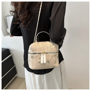 Detail of beige straw vanity bag featuring green floral embroidery and metal chain strap