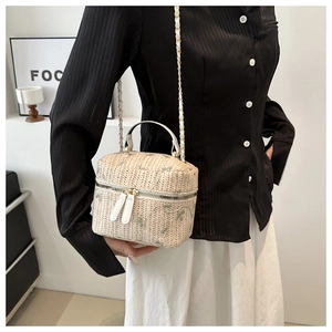 Straw box bag with green floral embroidery and chain strap worn by a model