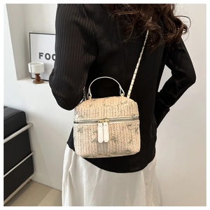 Detail of straw bucket bag featuring green floral embroidery and metal chain strap