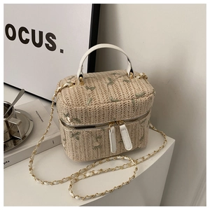 Macro view of woven straw box bag featuring green floral embroidery and white leather handle