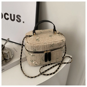 Detail of floral embroidery on beige straw bucket bag with black leather handle