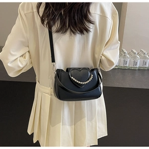 Detail of black crossbody bag featuring a 3D heart-shaped flap and faux pearl metal chain