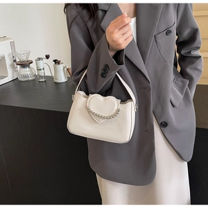 Detail of a creamy white crossbody bag with a heart flap and silver beaded chain strap