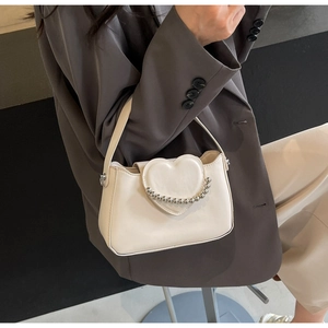 Detail of cream white leather handbag featuring heart-shaped flap and silver beaded chain