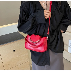 Detail of red heart crossbody bag with metal bead accents and dual strap design