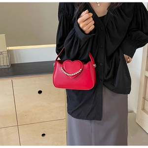 Detail of red heart-shaped flap handbag featuring delicate bead accents and a top handle