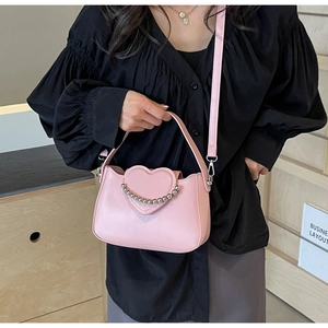 Close-up of pink crossbody bag with heart-shaped flap and silver beaded chain detail
