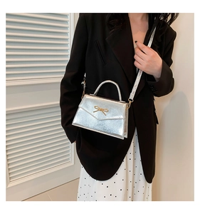 Détail du mini sac bandoulière argenté avec nœud doré porté par un mannequin élégant
