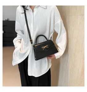 Détail d'un sac à bandoulière noir avec nœud doré sur fond de chemise blanche