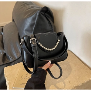 Detail of black handbag with heart flap and silver bead trim on stone surface