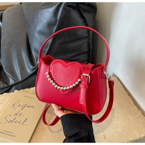 Detail of red faux leather handbag with heart flap and silver bead chain on a table
