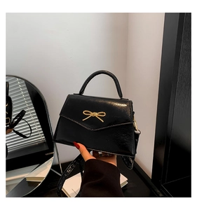 Détail d'un mini sac à main noir avec noeud doré et texture de cuir brillant
