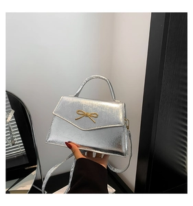 Détail d'un mini sac à main argenté avec une décoration de nœud en chaîne dorée et fini brillant