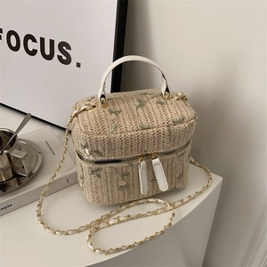Straw box handbag with green floral embroidery and white leather handles in a chic setting