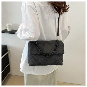 Detail of black quilted denim shoulder bag with chain strap worn by a model