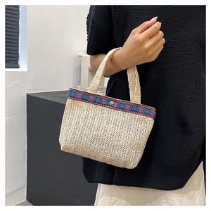 Detail of woven straw envelope bag featuring ethnic pattern trim and snap button closure
