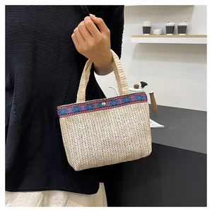 Detail of woven straw handbag featuring ethnic embroidery trim and secure metal snap closure
