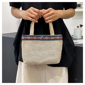 Detail of woven straw handbag featuring ethnic embroidery strap and round metal buckle