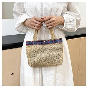 Detail of woven straw clutch with ethnic embroidery trim and silver metal snap button