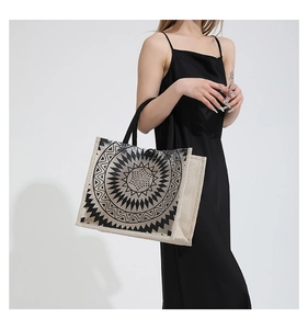 Detail of canvas tote bag with black mandala pattern held by model in black dress