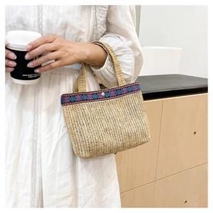 Macro view of hand-woven straw bag featuring ethnic embroidery and silver metal buckle