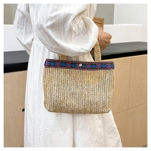 Detail of woven straw envelope bag with ethnic geometric pattern ribbon and magnetic snap