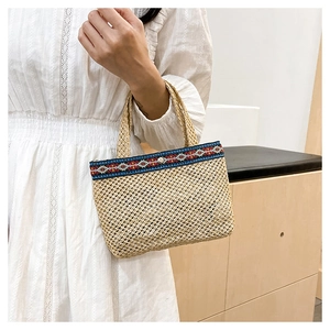 Detail of woven straw envelope bag featuring ethnic geometric ribbon and metal snap closure