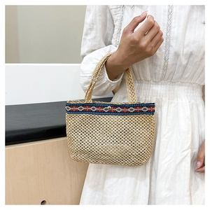 Detail of hand-woven straw clutch bag featuring ethnic embroidery and dual handles