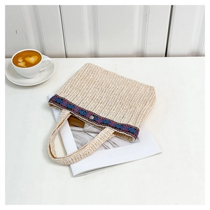 Close-up of beige straw woven clutch featuring ethnic embroidery and metallic snap button