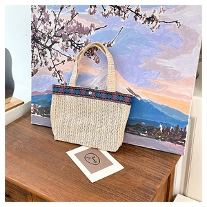 Detail of hand-woven straw bag with ethnic embroidered trim and silver metal lock closure