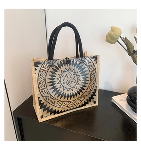 Detail of waterproof PVC tote bag with sun patterns and woven handles on a wooden table