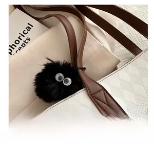 Close-up of black furry soot sprite bag charm with big eyes on white quilted tote bag
