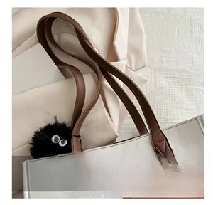 Detail of quilted tote bag featuring leather handles and a fuzzy decorative charm