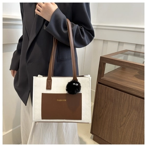 Detailed view of bicolor tote bag with brown pocket and plush eye charm on a model