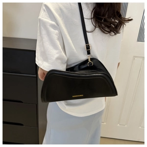 Détail d'un sac bandoulière noir en forme de croissant porté à l'épaule de côté