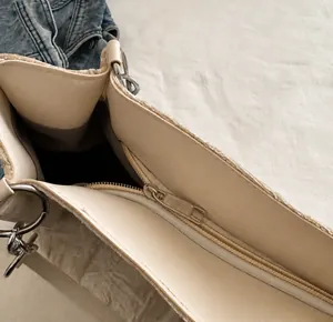 Detail view of the smooth zipper closure and metal ring on a beige tote bag