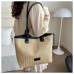 Detail of woven straw tote bag featuring black leather handles and knot strap design
