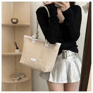 Detailed close-up of straw tote bag with white leather trim and knotted handle details